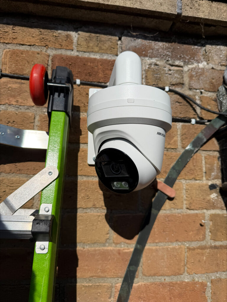 Hikvision CCTV camera mounted on a brick wall to provide coverage across a larger outdoor area.